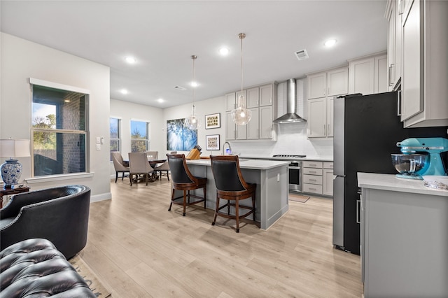 kitchen featuring light countertops, wall chimney exhaust hood, range, and a breakfast bar