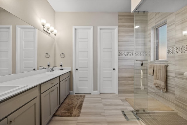 full bathroom with tiled shower, double vanity, baseboards, and a sink