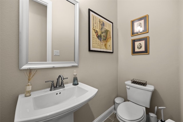 half bath with tile patterned flooring, baseboards, a sink, and toilet