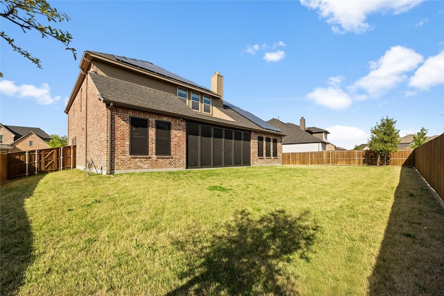 rear view of property with a yard, a fenced backyard, solar panels, and brick siding