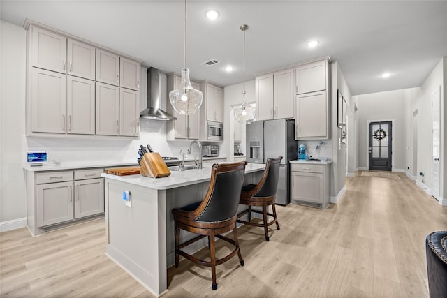 kitchen with light wood-style floors, a kitchen bar, wall chimney range hood, light countertops, and stainless steel appliances
