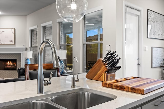 room details with a tiled fireplace, decorative light fixtures, a sink, and light stone counters