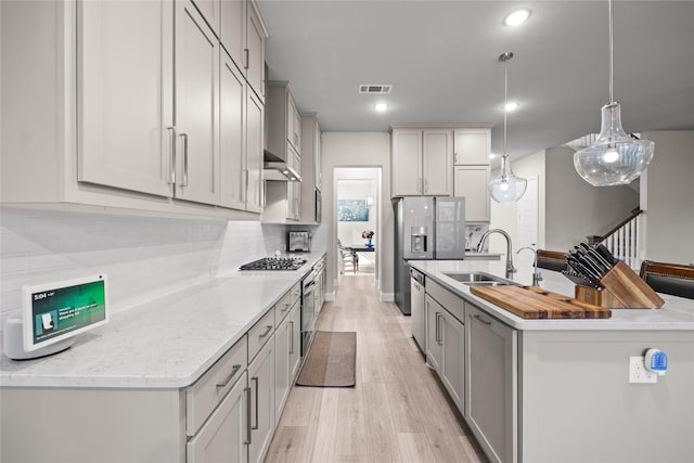 kitchen with an island with sink, gray cabinetry, visible vents, light wood finished floors, and a sink