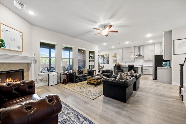 living room with light wood-style flooring, a ceiling fan, visible vents, a tile fireplace, and baseboards