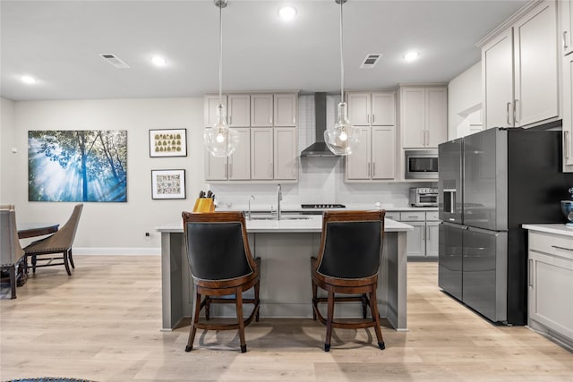 kitchen featuring wall chimney exhaust hood, stainless steel appliances, light wood finished floors, a breakfast bar area, and baseboards