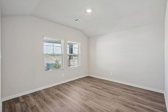 unfurnished room featuring baseboards, lofted ceiling, visible vents, and wood finished floors