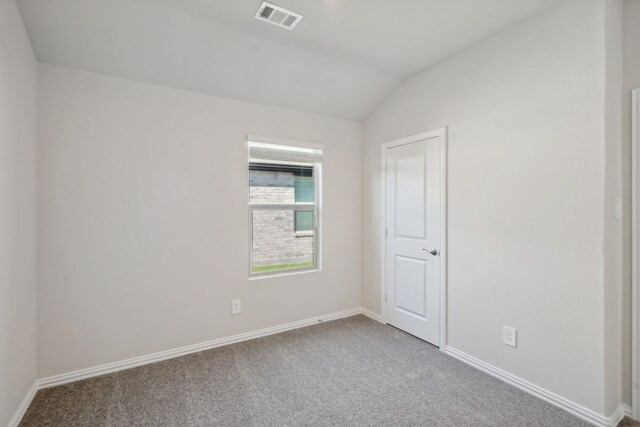 empty room featuring carpet flooring, baseboards, vaulted ceiling, and visible vents