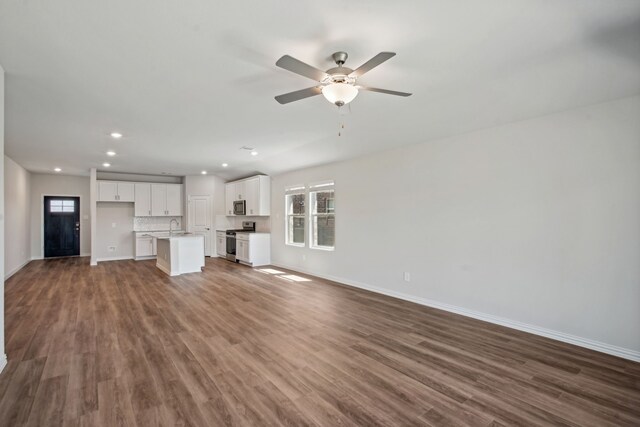 unfurnished living room with a sink, dark wood-style floors, baseboards, and ceiling fan