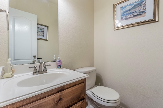 bathroom with a textured wall, vanity, and toilet