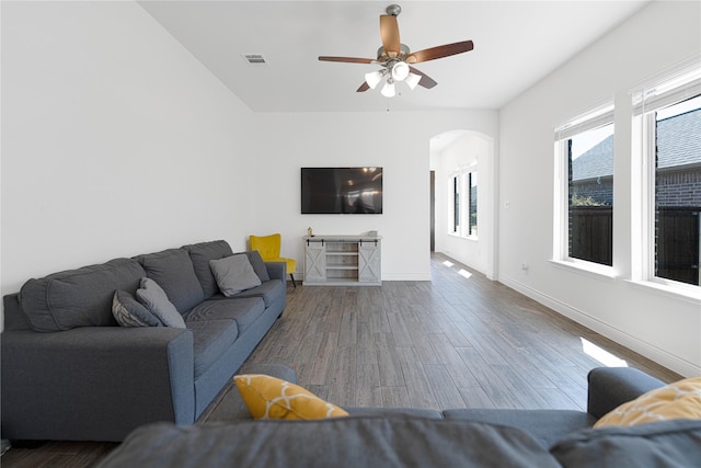 living area featuring baseboards, arched walkways, visible vents, a ceiling fan, and wood finished floors