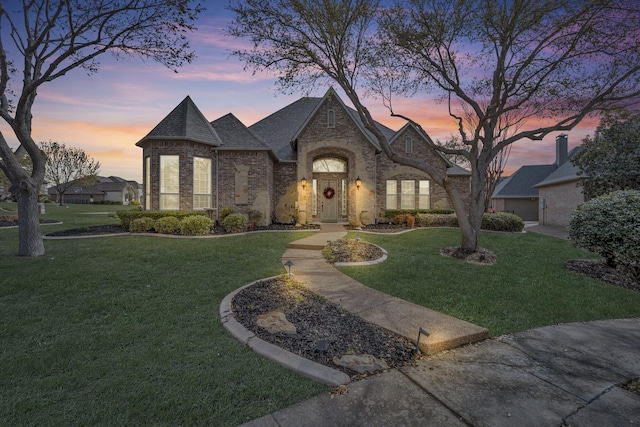 french country home with brick siding, a front yard, and roof with shingles