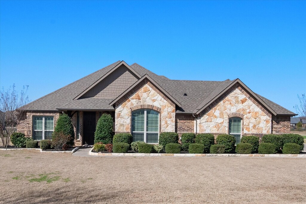 french provincial home featuring stone siding and roof with shingles