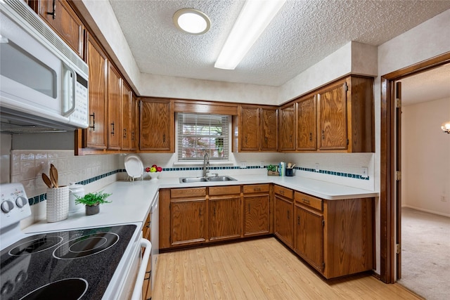 kitchen featuring light countertops, a sink, brown cabinets, electric stove, and white microwave
