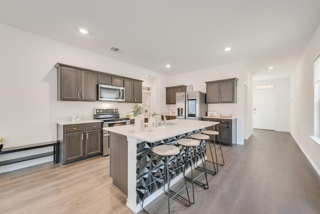 3213 Grimaldo Dr, Mesquite, TX 75126 - kitchen featuring appliances with stainless steel finishes, a breakfast bar, light countertops, light wood finished floors, and an island with sink