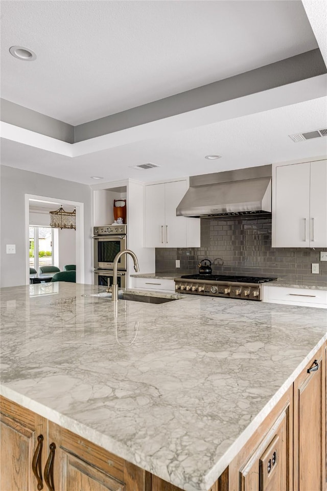 5230 Boca Raton Dr, Dallas, TX 75229 - kitchen with stainless steel appliances, backsplash, visible vents, light stone countertops, and wall chimney exhaust hood