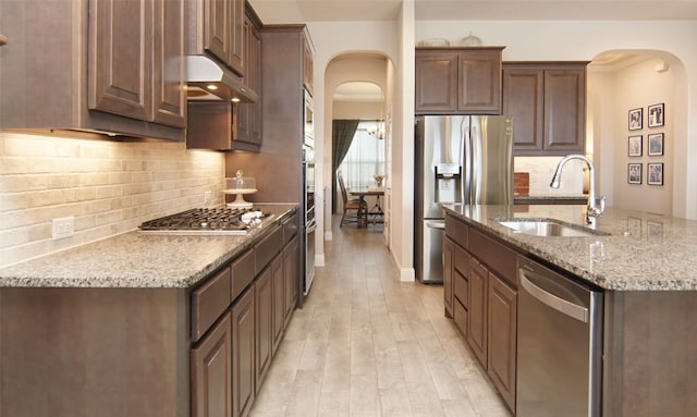 kitchen with stainless steel appliances, under cabinet range hood, a sink, arched walkways, and light wood finished floors