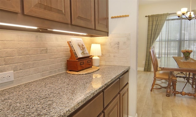 interior space featuring light stone counters, tasteful backsplash, baseboards, light wood-style floors, and an inviting chandelier