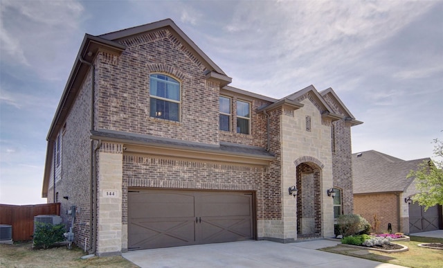 french country home featuring stone siding, an attached garage, concrete driveway, brick siding, and cooling unit