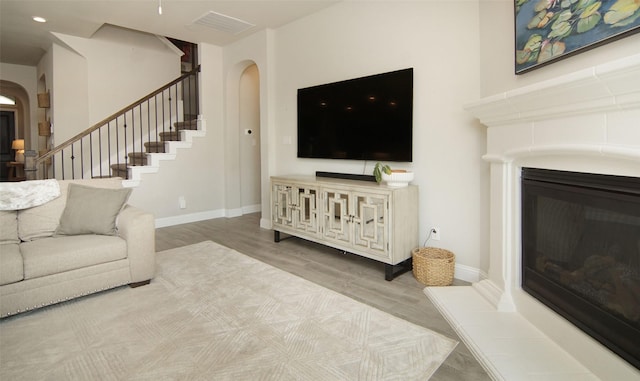 living room with stairs, arched walkways, visible vents, a glass covered fireplace, and wood finished floors