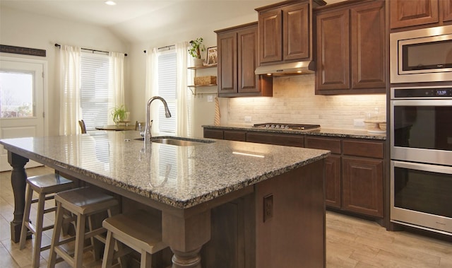 kitchen with a sink, open shelves, tasteful backsplash, appliances with stainless steel finishes, and under cabinet range hood