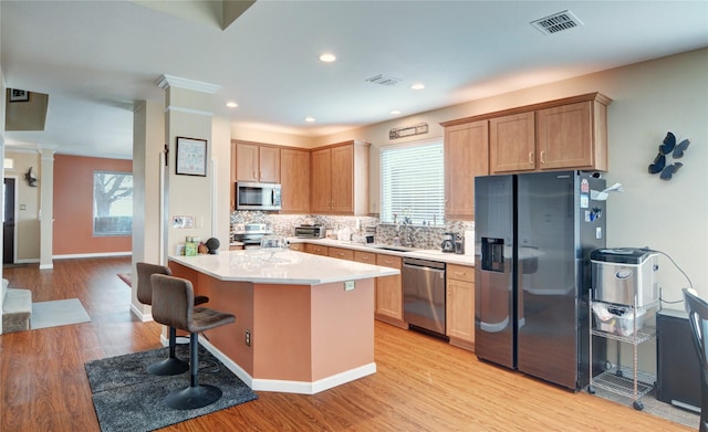 kitchen with light countertops, ornate columns, stainless steel appliances, decorative backsplash, and a sink