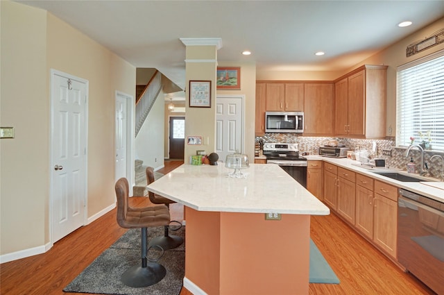 kitchen featuring a sink, light wood finished floors, tasteful backsplash, a kitchen breakfast bar, and appliances with stainless steel finishes