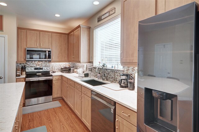 kitchen featuring stainless steel appliances, backsplash, a sink, light wood finished floors, and light brown cabinets