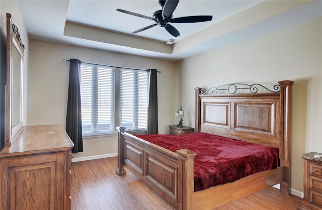 bedroom with a tray ceiling, baseboards, and light wood-style floors