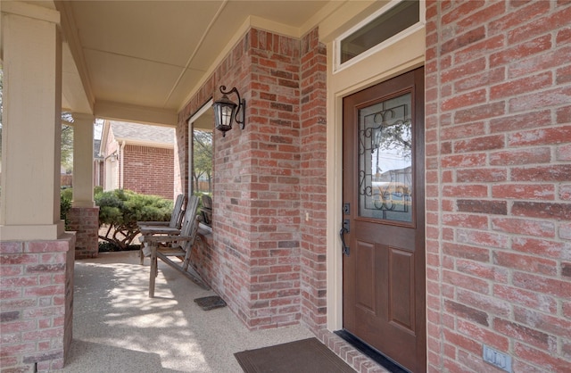 view of exterior entry featuring a porch and brick siding