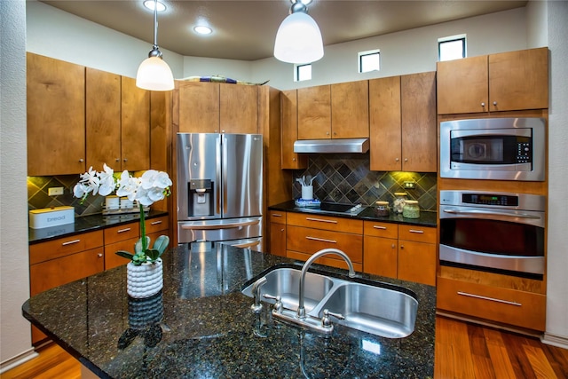kitchen with brown cabinets, under cabinet range hood, stainless steel appliances, and a sink
