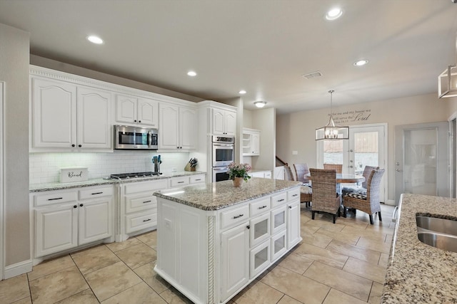 820 Clearlake Dr, Prosper, TX 75078 - kitchen with appliances with stainless steel finishes, a chandelier, backsplash, white cabinets, and pendant lighting