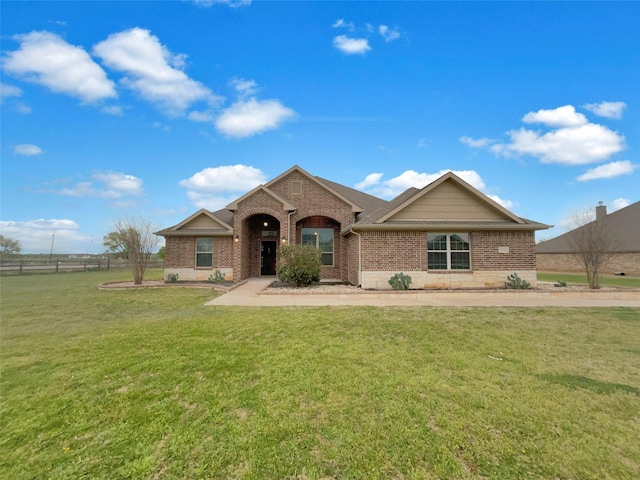 view of front facade featuring roof with shingles, brick siding, a front yard, and fence
