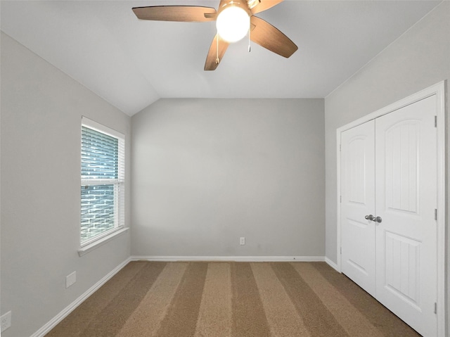unfurnished bedroom with lofted ceiling, carpet flooring, baseboards, a ceiling fan, and a closet