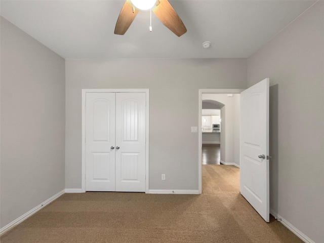 unfurnished bedroom with a closet, carpet flooring, a ceiling fan, baseboards, and arched walkways
