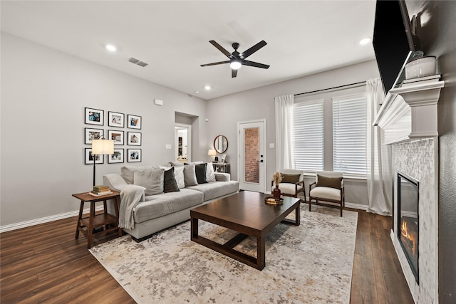 living room with ceiling fan, visible vents, baseboards, a tiled fireplace, and dark wood-style flooring
