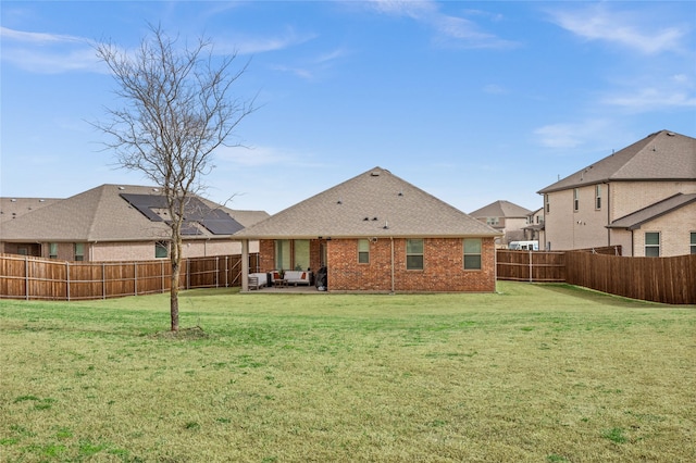 rear view of house featuring outdoor lounge area, a fenced backyard, roof with shingles, a lawn, and brick siding