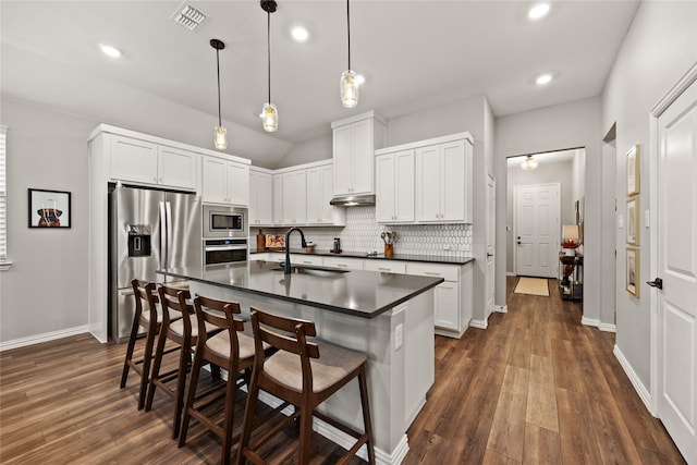 kitchen with dark countertops, a sink, stainless steel appliances, under cabinet range hood, and visible vents
