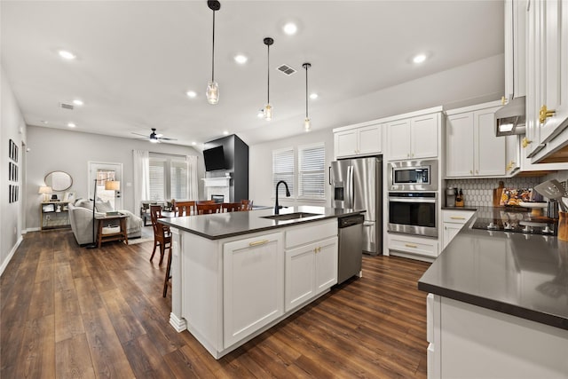 kitchen featuring open floor plan, dark countertops, stainless steel appliances, and a sink