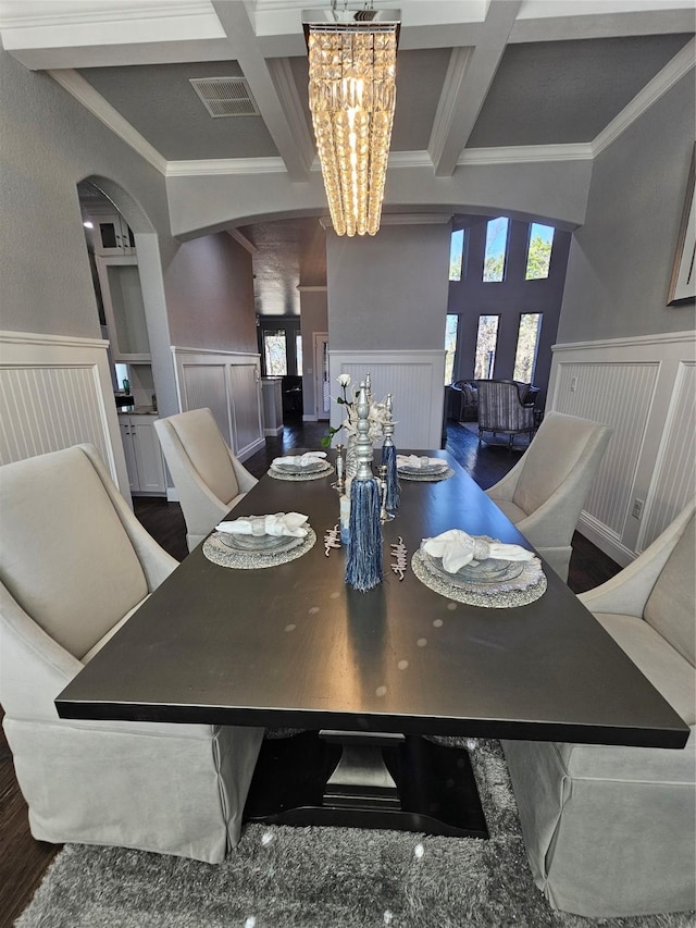 dining room featuring ornamental molding, a notable chandelier, coffered ceiling, and a decorative wall