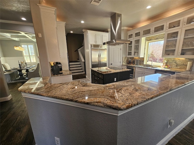 kitchen featuring a sink, island range hood, stainless steel appliances, light stone countertops, and dark wood-type flooring