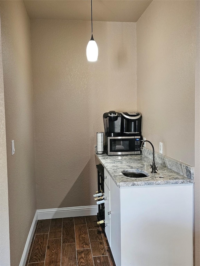 kitchen featuring wood tiled floor, a sink, stainless steel microwave, light stone countertops, and baseboards