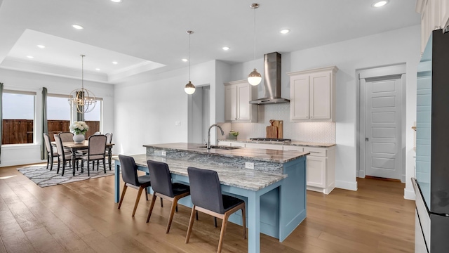 1651 Wynne Ave, Prosper, TX 75078 - kitchen with wall chimney range hood, a sink, light wood-style floors, a tray ceiling, and decorative backsplash