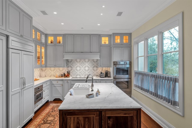 kitchen with crown molding, a sink, paneled fridge, stainless steel double oven, and visible vents
