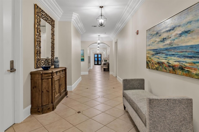 corridor featuring light tile patterned floors, ornamental molding, baseboards, a chandelier, and arched walkways