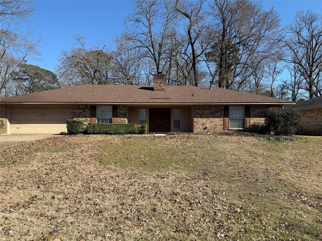 single story home featuring a chimney, brick siding, concrete driveway, and an attached garage