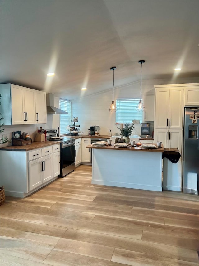 kitchen with white cabinetry, appliances with stainless steel finishes, lofted ceiling, wall chimney range hood, and light wood-style floors