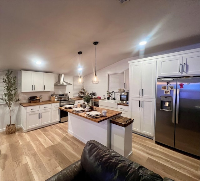 kitchen featuring a sink, light wood finished floors, wall chimney exhaust hood, stainless steel appliances, and wood counters