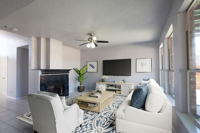 living room with a premium fireplace, tile patterned floors, a ceiling fan, baseboards, and a textured ceiling