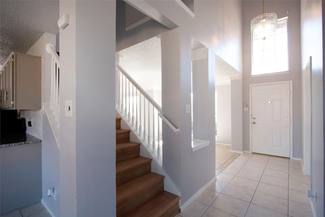 entrance foyer with light tile patterned floors, stairway, baseboards, a notable chandelier, and a high ceiling