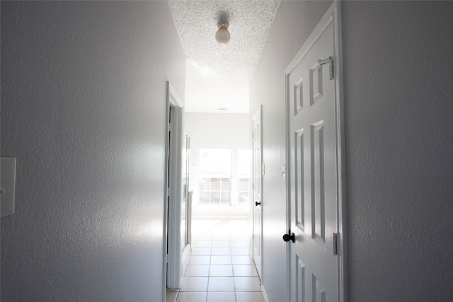 hallway with light tile patterned floors, a textured ceiling, and a textured wall
